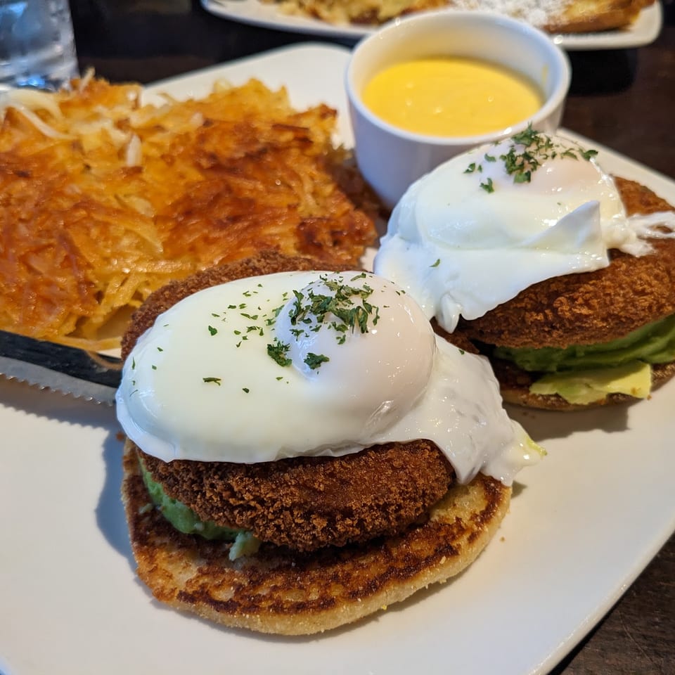 Two avocado benedicts with poached eggs, hash browns, and a side of hollandaise sauce.